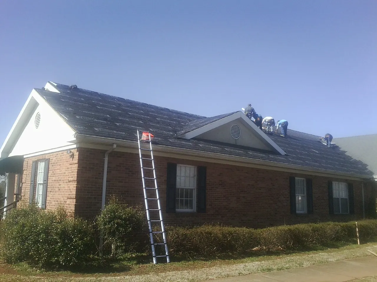 Crew tearing shingles off a brick ranch roof with a ladder set — Metal Roof Repair work by our crew in Springfield