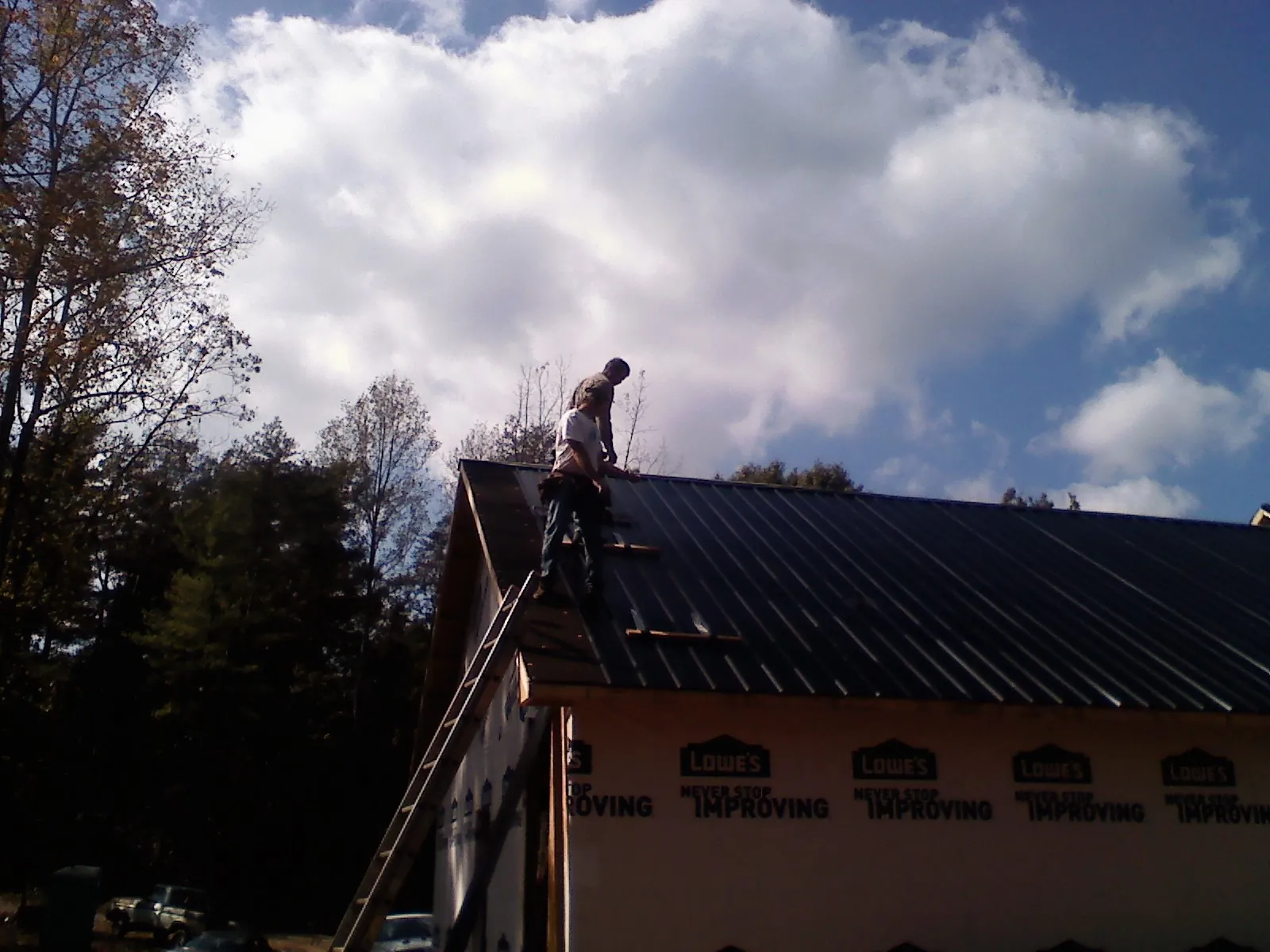 Roofer fastening dark metal panels high against a cloudy sky, from a Roof Inspection job in Springfield